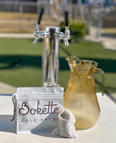 pictured is a select coffee bean pouch with a yellow glass pitcher atop the Boketto bicycle vending cart